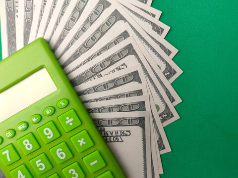 A bright green calculator is placed beside a fan of United States dollar bills on a green background