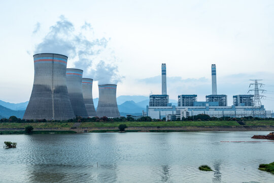large thermal power plant cooling towers by the river emitting smoke