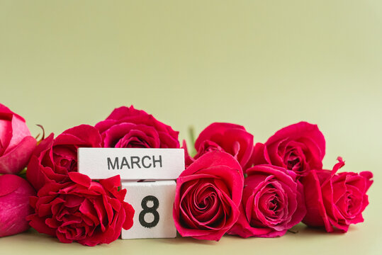 Fresh red roses arranged around wooden block calendar displaying March 8 on light background. Vibrant flowers and minimalist calendar create elegant composition celebrating International Women's Day
