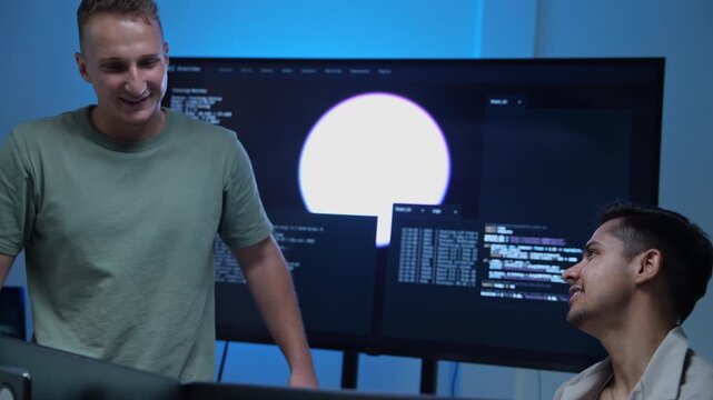 Two AI engineers are collaborating in a modern workspace, discussing software development and digital data on a large computer screen for an advanced technology project.