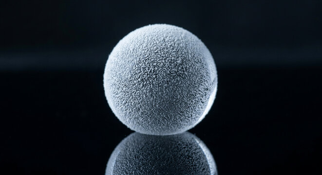 Spherical liquid marble water droplet coated in fine white hydrophobic lycopodium powder resting on reflective black surface, physics fluid dynamics science experiment macro photography