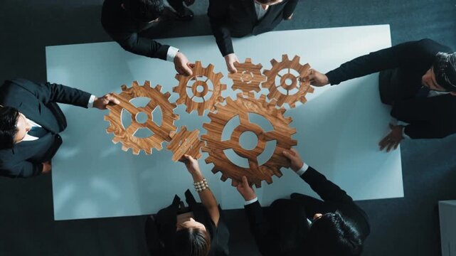 Top view of professional business team bring filled last cog to complete system. Group of smart diverse business people joining gear together at workplace.Show teamwork,unity, working. Directorate.