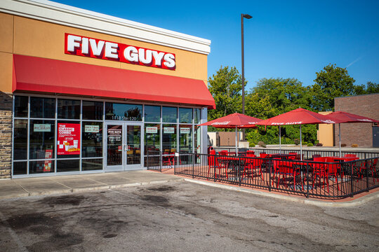 O&rsquo;Fallon, Illinois, USA &mdash; August 29, 2025: Wide exterior view of a Five Guys restaurant and its outdoor seating area, with red umbrellas and tables beside the storefront.