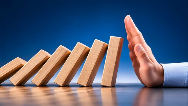 Hand stopping falling dominoes to prevent chain reaction concept of risk management crisis intervention and problem solving in business and life