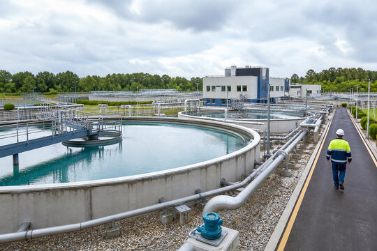 Water treatment plant with circular clarifiers, pipelines and an operator walking through the facility, illustrating modern municipal water management.