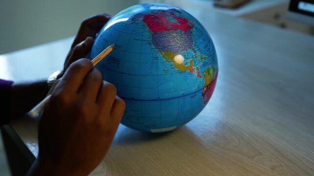 Child learning geography with a world globe, Child's hands use a pencil to point at a colorful world globe on a wooden table, showing geography learning and travel planning.