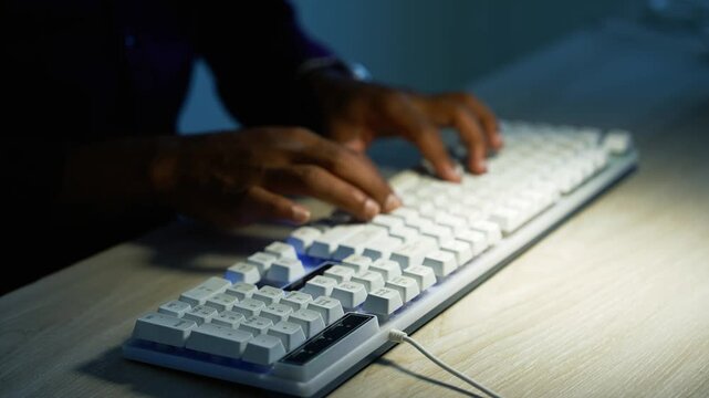 Hand typing on a white computer keyboard, Close-up of a white computer keyboard on a wooden desk with a hand reaching to type in low light, creating a focused evening work atmosphere.