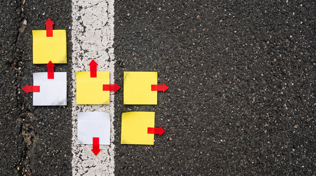 Top view of blank sticky notes with red arrow markers pointing different ways on asphalt beside faded lane line, crossroads decision concept 