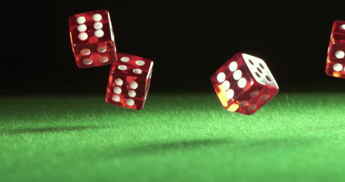 Close up slow motion video of five red clear dice falling and bouncing on green felt table in a dynamic casino shot.