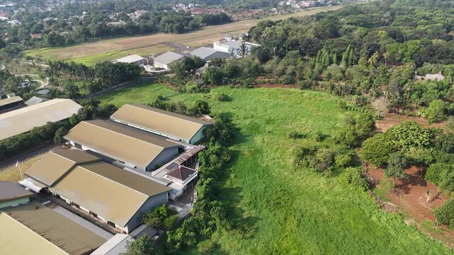 Workers are erecting a new building at the construction site. A dirt road winds across the area. Vehicles are parked nearby. Green grass and construction materials are visible there and along the road