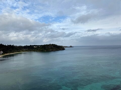 Calm turquoise bay and green headland under an overcast morning sky in Okinawa, Japan