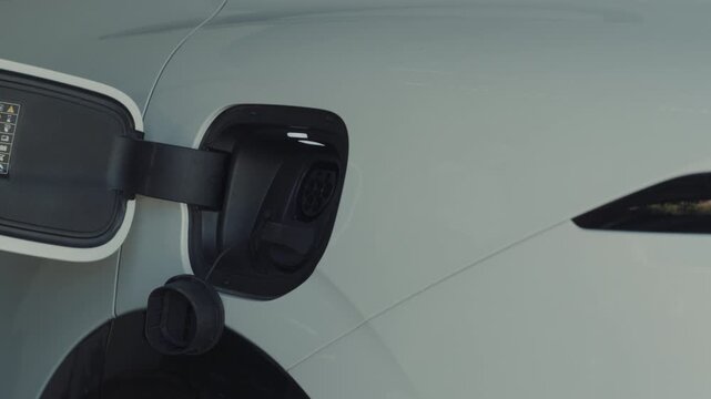 Person plugging in EV charging cable to white electric vehicle for sustainable energy transport.	
