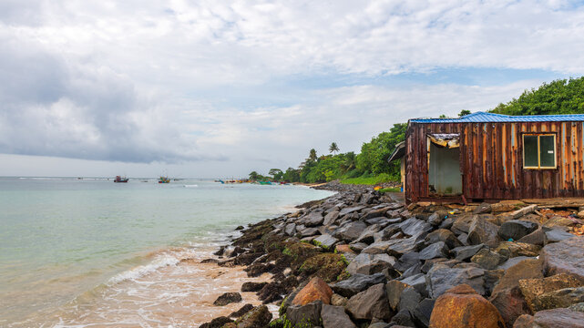 A weathered container shelter on a rocky shoreline beside calm tropical waters at weligama harbour, sri lanka.