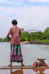 Fototapeta premium Traditional fisherman fishing from a coastal pier, viewed from behind in Weligama, Sri Lanka