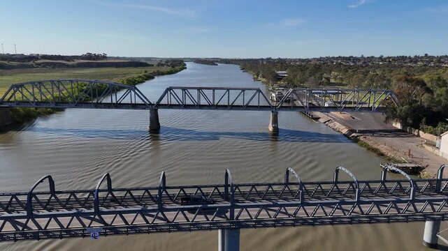 Aerial view of the historic parallel steel truss bridges crossing the wide Murray River at Murray Bridge, South Australia with the regional township and riverbanks. Engineering infrastructure