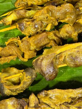 Close up Indonesian chicken gizzard skewers sate ampela braised in turmeric yellow spices, arranged neatly on fresh green banana leaf food background
