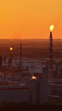 Aerial trucking shot of oil refinery in Plock, Poland at golden sunset with gas flare stack burning above storage tanks, pipelines and chimneys of vast petrochemical plant