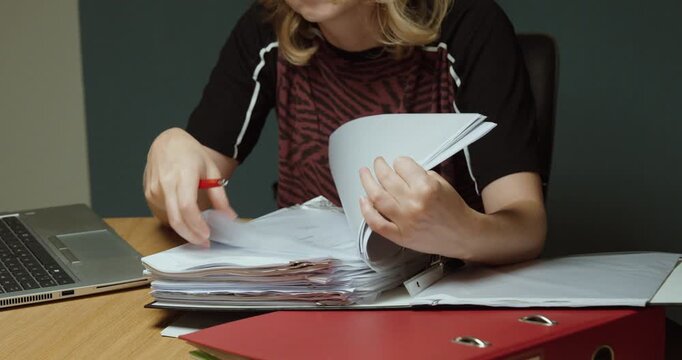 Woman flipping through a large stack of paperwork while working at a desk.