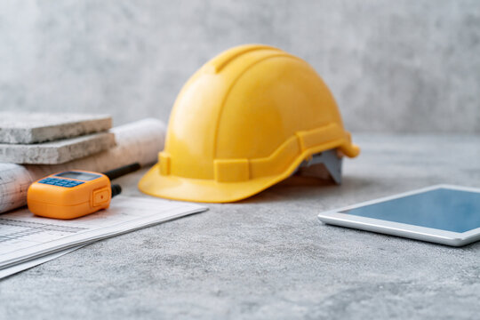 Yellow hard hat rests beside tools and a tablet. Construction plans lie open nearby. Scene suggests planning or pause during work. Ideal for building, engineering, or project management visuals