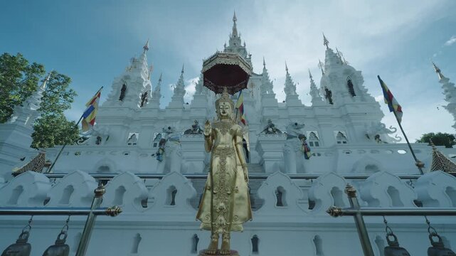 Golden standing Buddha under a tiered parasol before a white temple