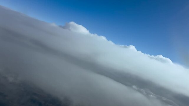 Immersive pilot eye view in a left turn breaking into a layer of ethereal stratus clouds under a blue sky. scene captured from a jet cockpit at cruise in the upper atmosphere. 4K