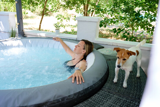 Woman relaxing in outdoor hot tub with dog beside her