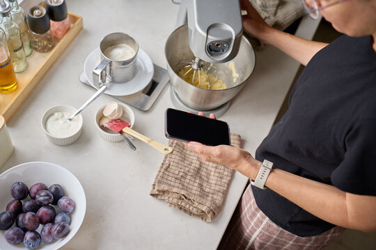 Woman using smartphone beside stand mixer in kitchen