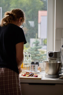 Woman slicing plums for a cake by the kitchen window