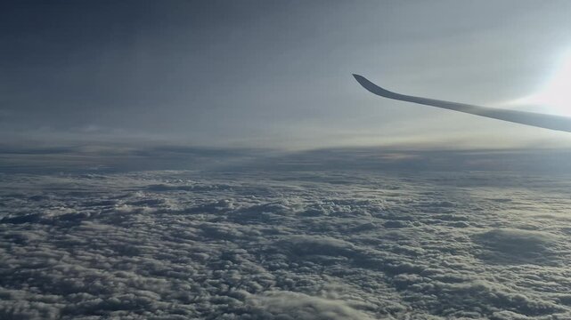 Window seat view of airplane wing flying high above seemingly endless expanse of textured white clouds in atmosphere