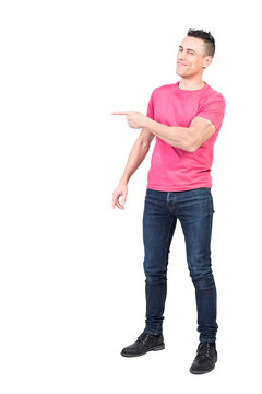 Full body of positive male model in casual clothes pointing aside while standing isolated in light studio