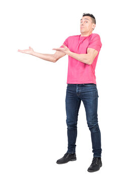 Full body of confused male model in casual outfit pointing aside and looking at camera with amazed face
