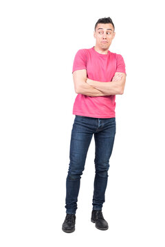 Full body of astonished male in casual clothes looking into distance while standing with crossed arms