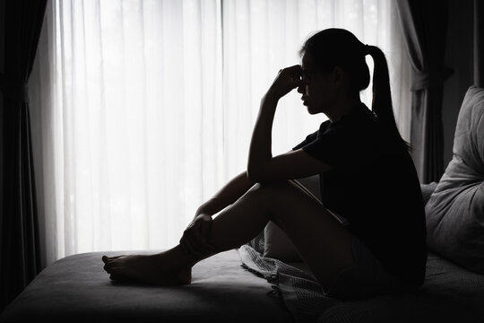  Silhouette of woman sitting alone on bed