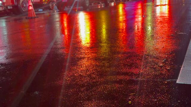 Cinematic low-angle shot of a fire truck and police car on a wet, rain-slicked street at night. Vibrant red and blue emergency lights reflect off the glossy asphalt, creating a.

