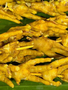 Fresh raw chicken feet skewered on wooden sticks for traditional Asian grilling, arranged on green banana leaf, top view close up food background