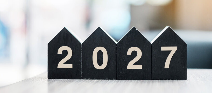 2027 Happy New Year with wooden Home model on table office. New House, Financial, Property insurance and real estate concepts