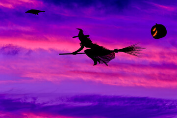 Fototapeta premium Halloween Silhouette of Witch Flying on Broomstick Against Vibrant Sunset Sky with Jack-O'-Lantern and Raven, Spooky Autumn Background
