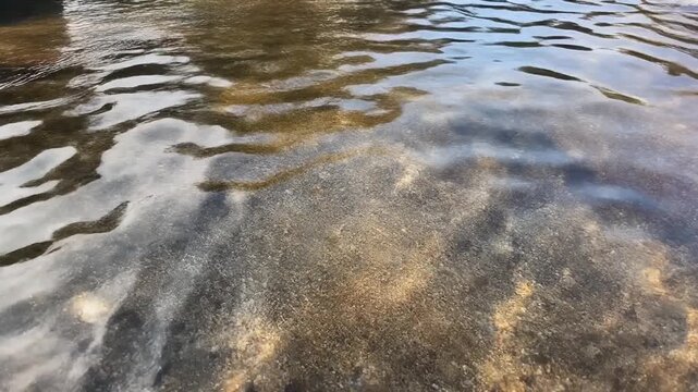 Clear river water flowing over a rocky riverbed with gentle ripples reflecting the daylight