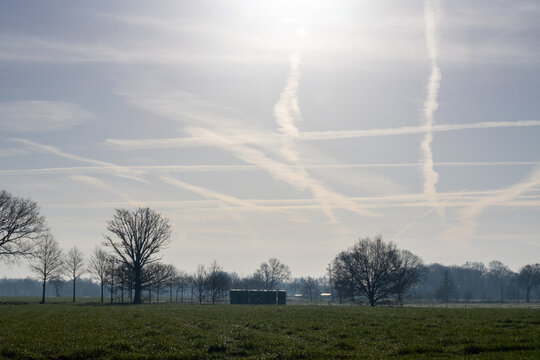 Multiple Aircraft Contrails Crossing Over Rural Winter Countryside Landscape Under Bright Sun