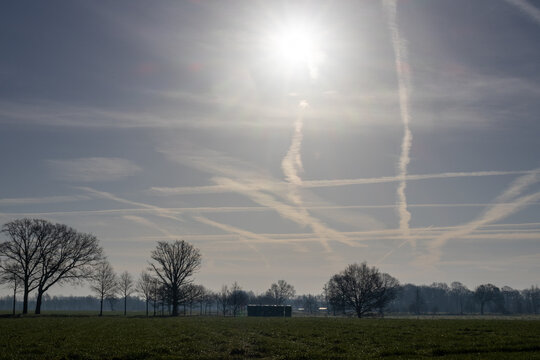 Multiple Aircraft Contrails Crossing a Dramatic Sunlit Sky Over Rural Countryside Landscape