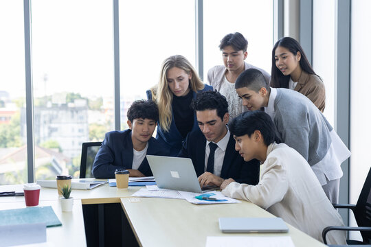 Diverse business team looking at laptop computer screen in modern office boardroom showing focused and happy expression during collaboration