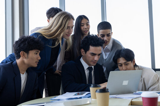 diverse professional team engaged in business meeting looking at laptop screen inside modern office workplace environment