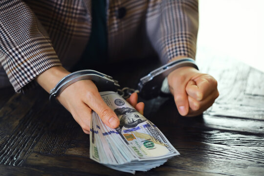 women's handcuffed hands hold dollars on a dark wooden background