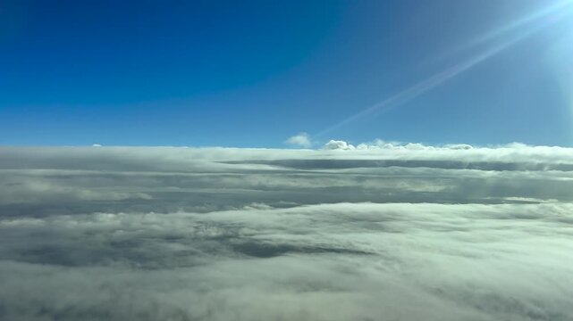 Cockpit View flying over an ethereal layer of stratus clouds bathed in by the sunlight, with sun rays in the upper right corner. 4K