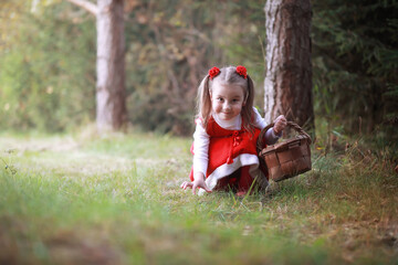 Obraz premium A little girl in a red hat and dresses is walking in the park. Cosplay for the fairytale hero 