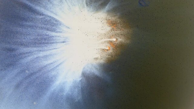 White ink erupts into a bright halo with blue rays and subtle orange wisps, creating a starburst-style macro background.
