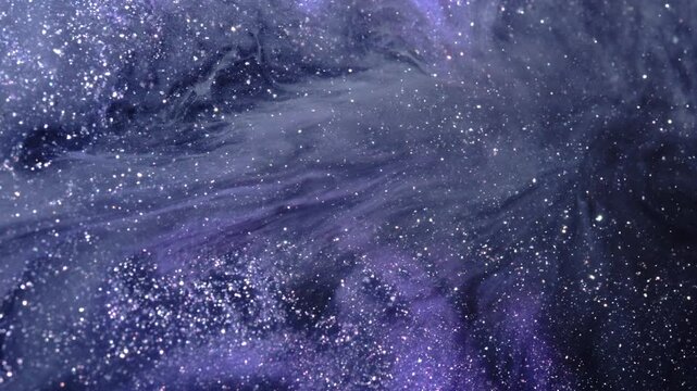 Dense glitter specks drift across swirling blue-violet ink, forming a space-like flowing texture in macro close-up.