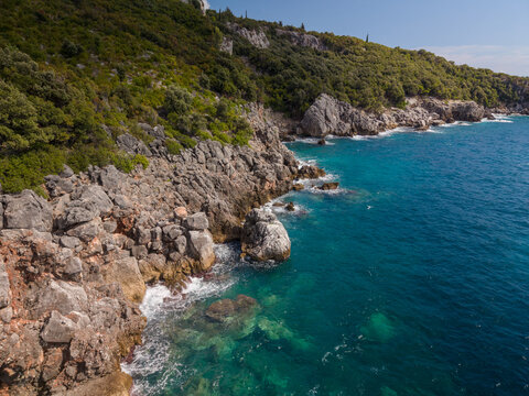 Aquarium bay Albania presents rugged rocky shoreline beside clear turquoise water. Green hillside rises above coast, and seaside setting feels peaceful, wild, and distinctly Mediterranean.