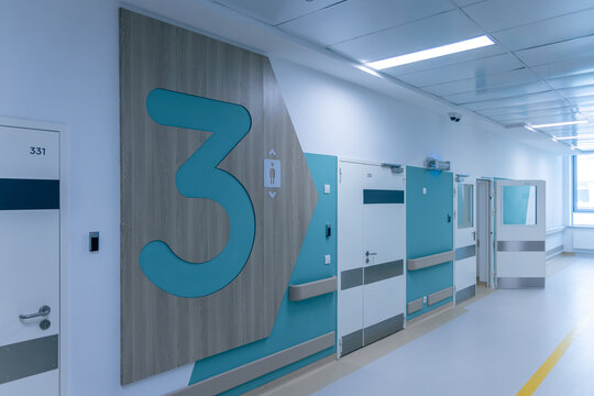 A huge number three with an elevator sign marks the third floor of a new hospital. Doors to rooms line the bright corridor. The bold floor design helps patients find their way quickly