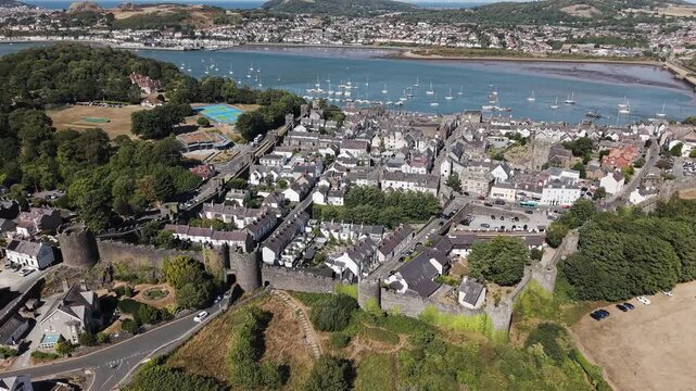 Medieval stone fortifications enclosing a coastal town in Wales, boats moored in calm estuary waters under clear sky